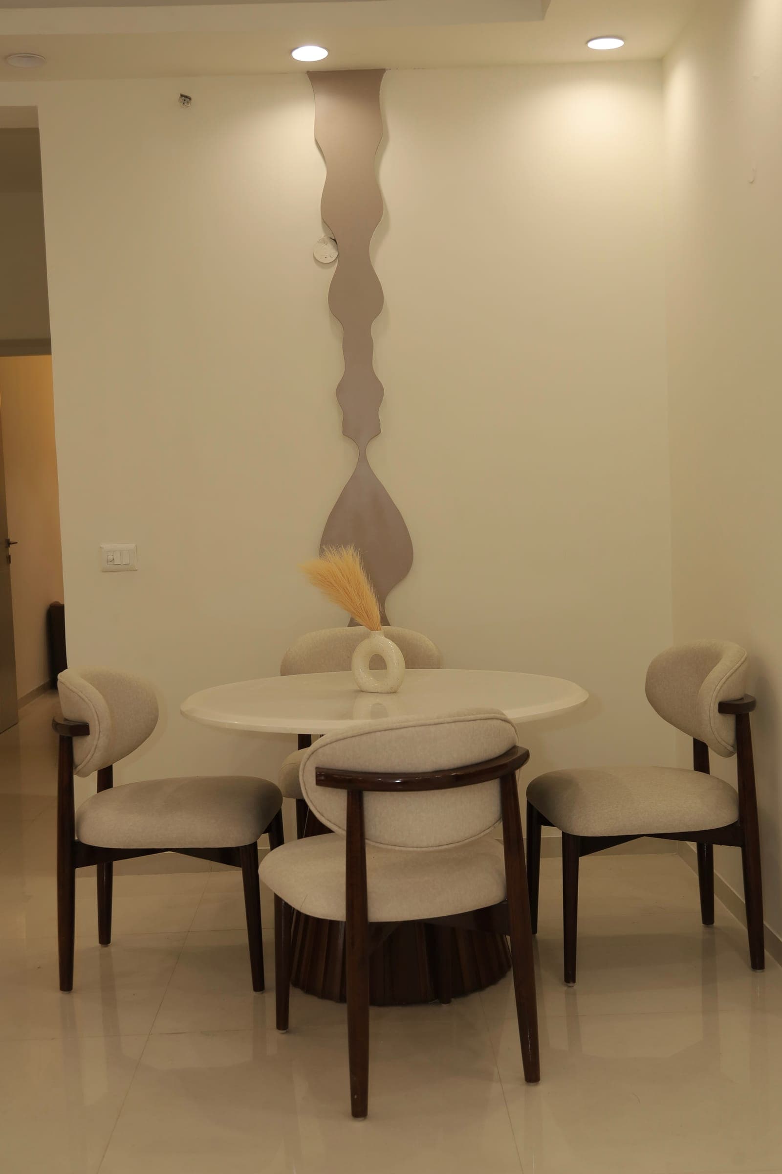 Dining nook with a round white table, dark-wood upholstered chairs and a wavy mirror strip on the wall.