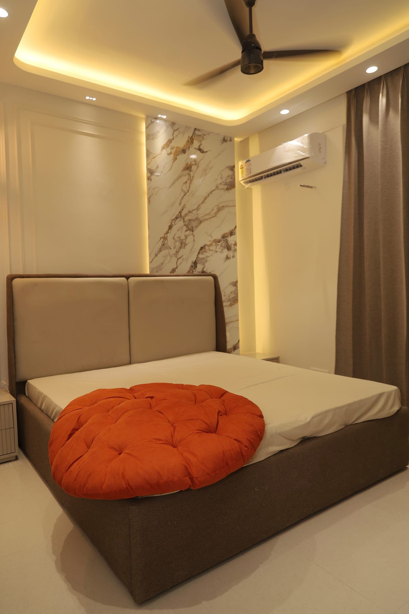 A calm bedroom with a grey upholstered bed and a veined marble accent wall