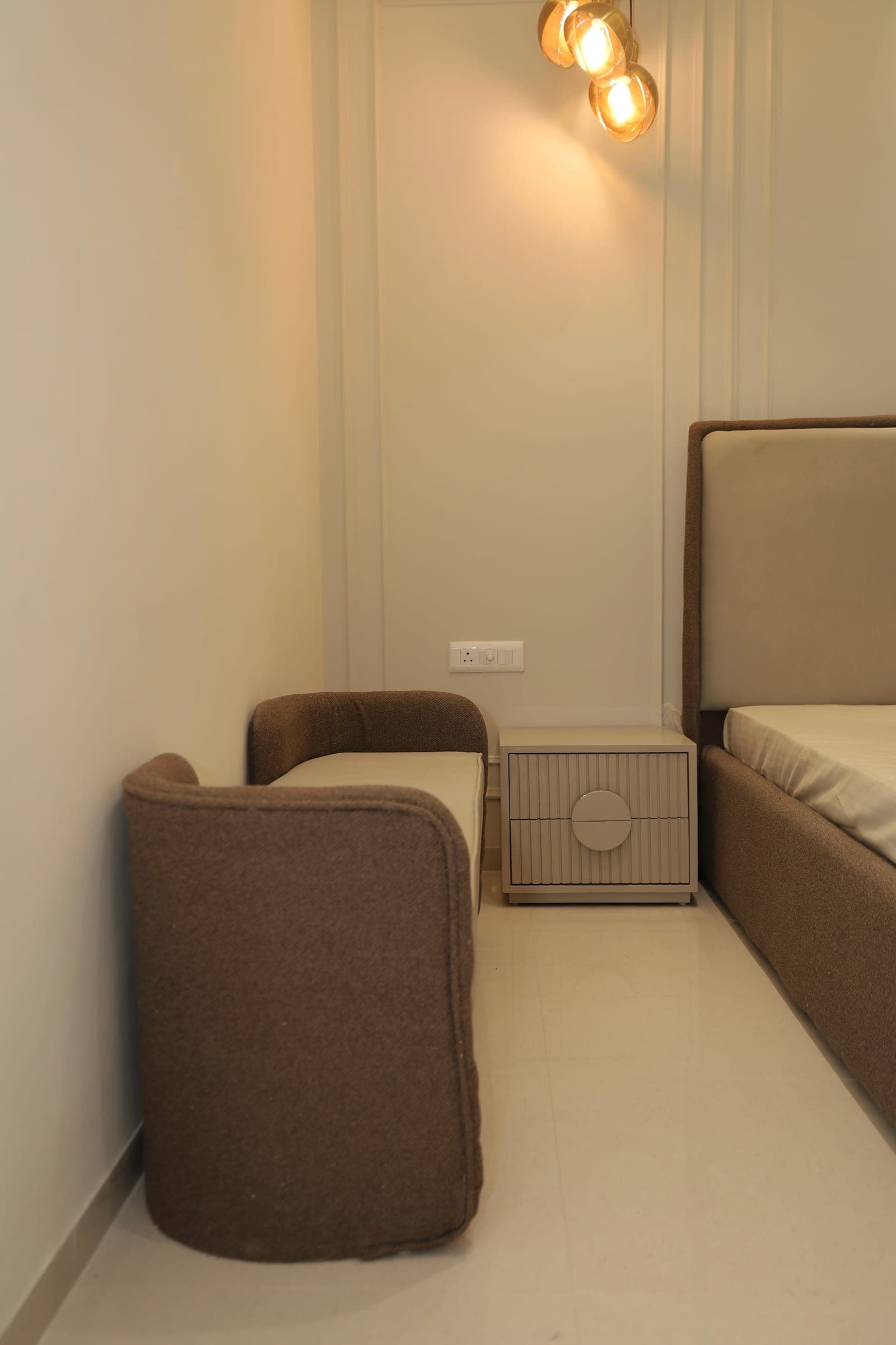 Bedroom corner with a brown boucle bench, a fluted bedside cabinet and warm glass globe pendant lights.