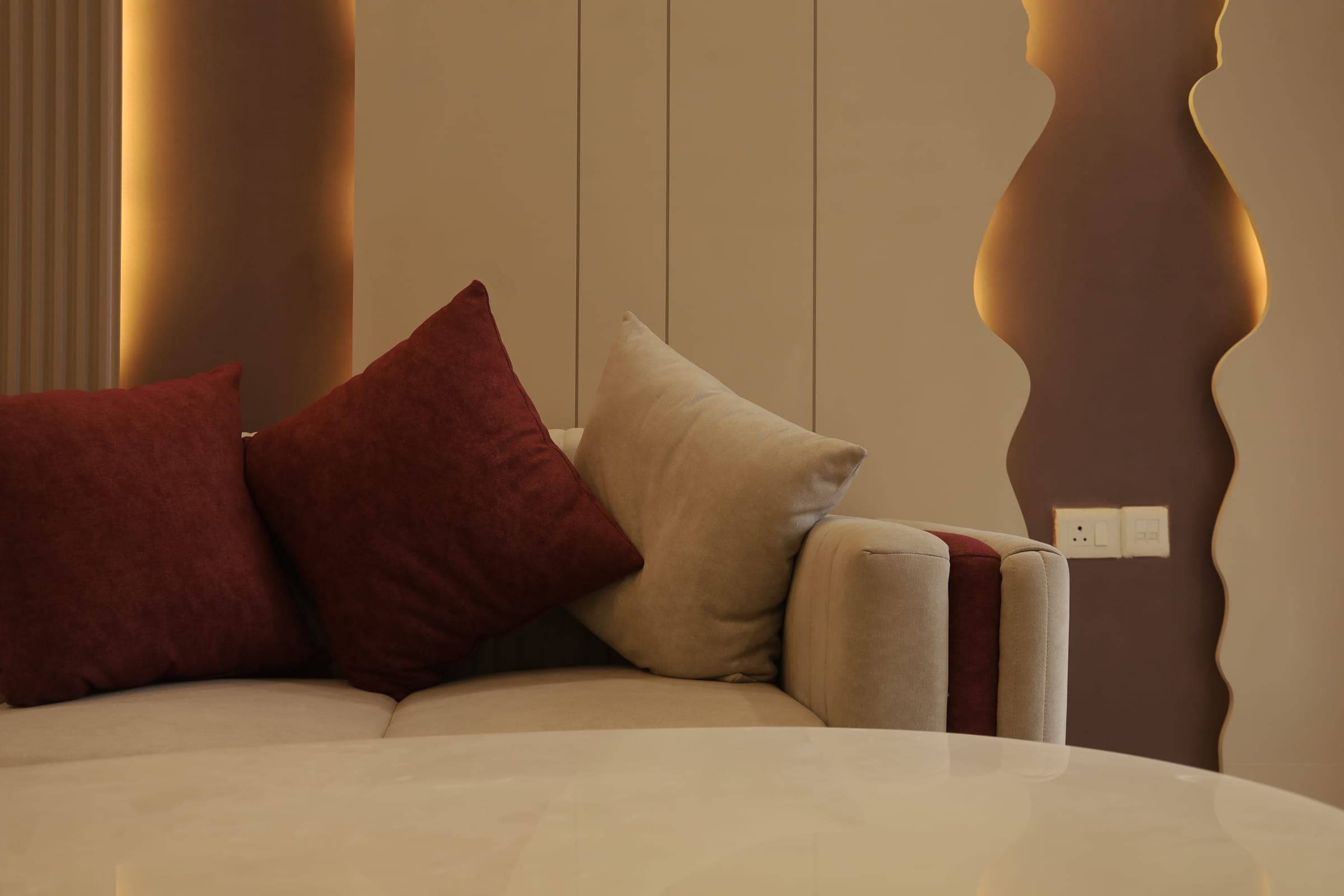 Close-up of a sofa with maroon and beige cushions against a fluted panel wall lit by warm accent lighting.