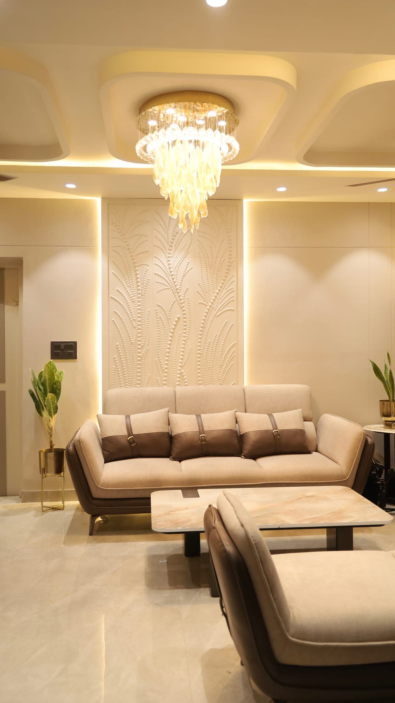 A considered living room with layered neutrals, a botanical feature panel and a glass chandelier