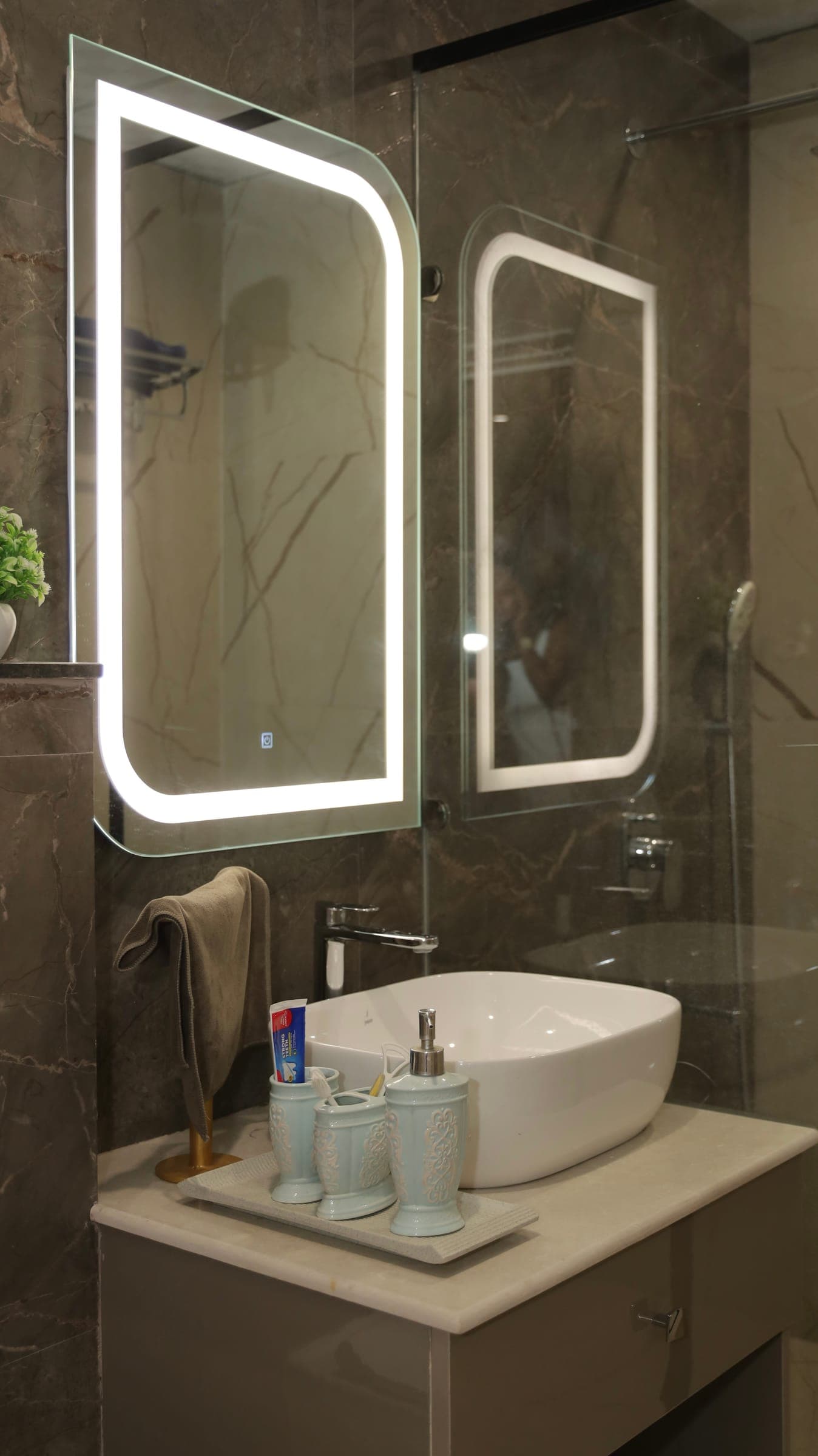 Bathroom vanity with a white countertop basin, chrome tap and two backlit LED mirrors against grey marble-look walls.