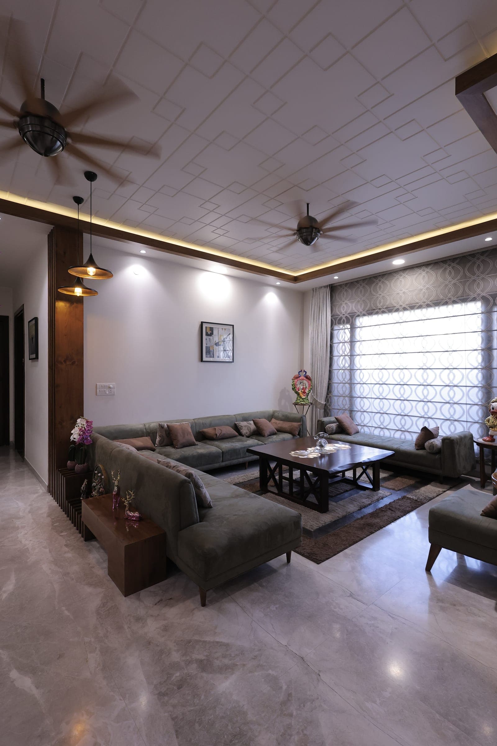 Living room seating with velvet sofas, a coffee table, framed wall art and a patterned white false ceiling with warm cove lighting.