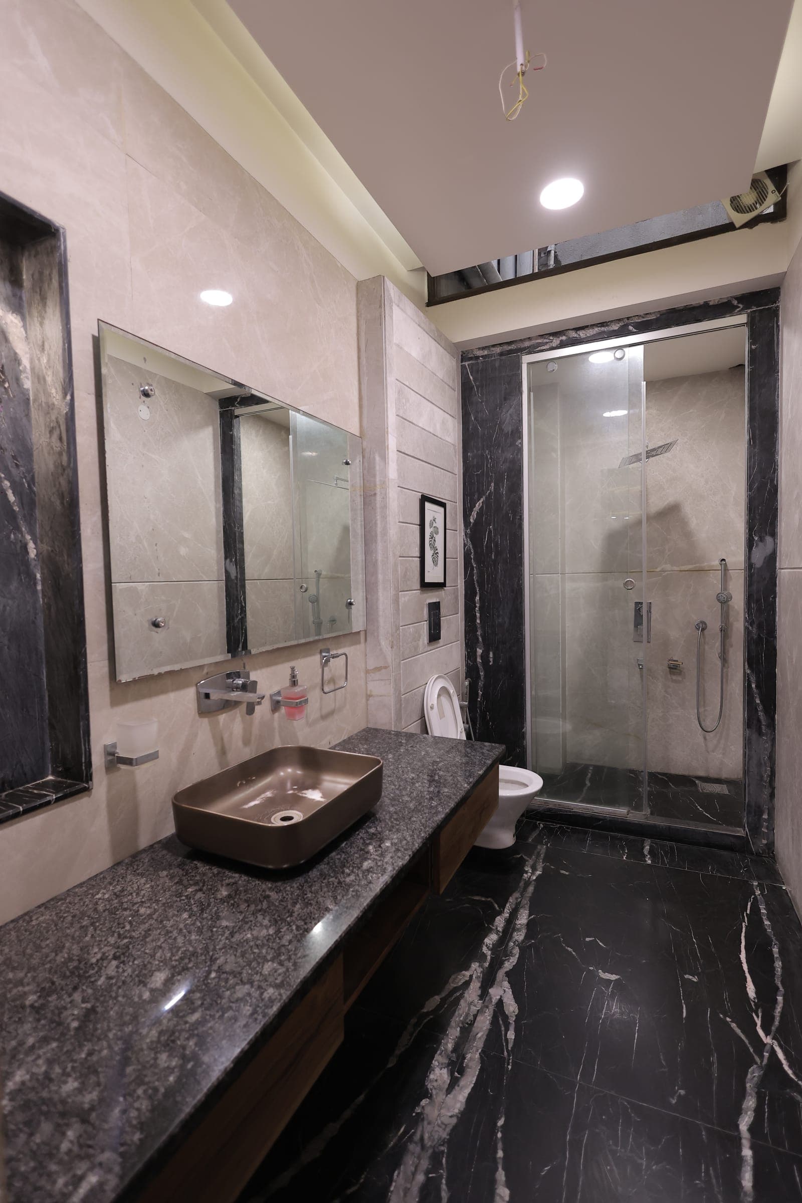 Bathroom with dark marble walls, a stone countertop, a bronze vessel basin and a glass-partitioned shower area.