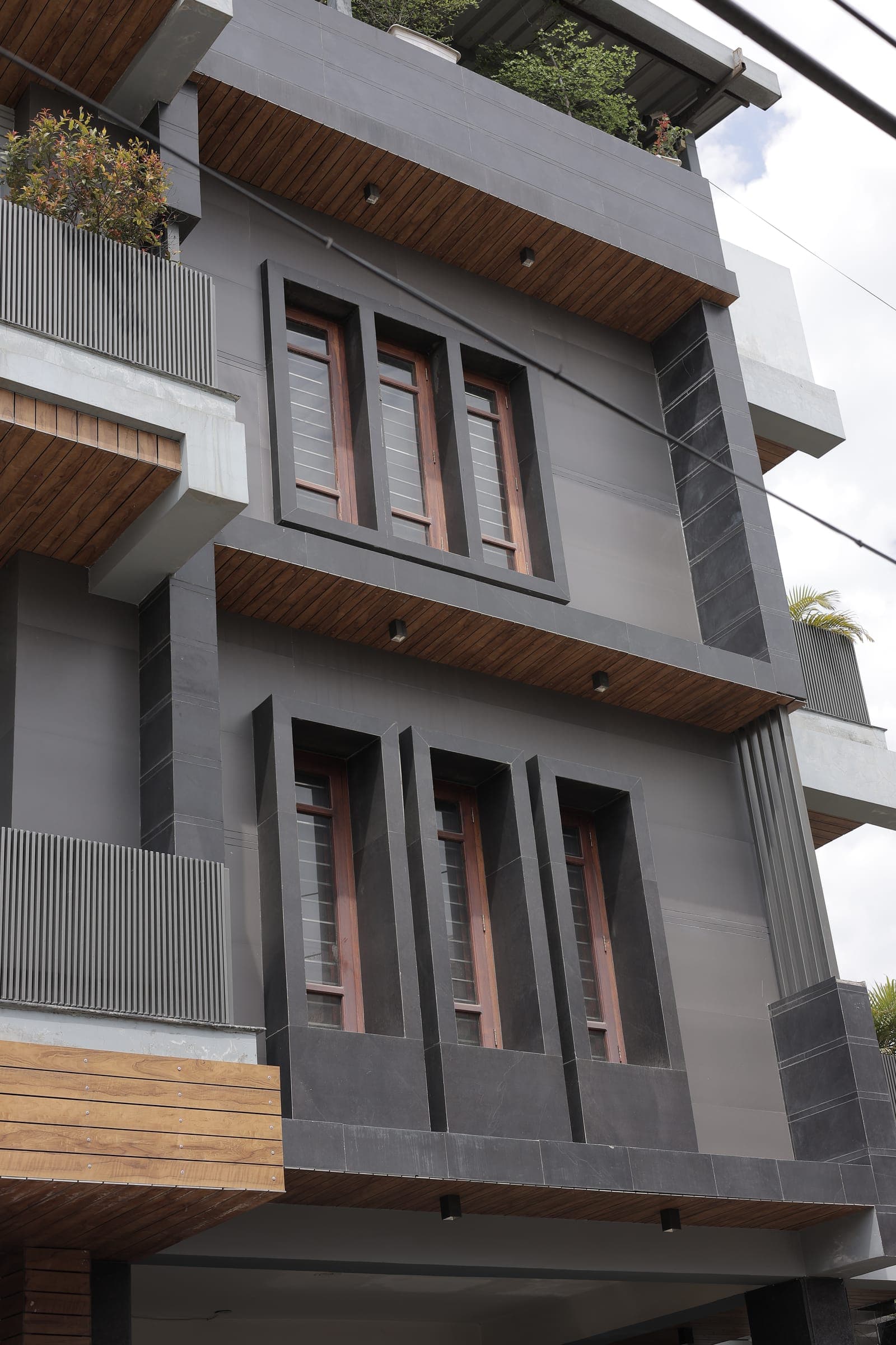 Close view of stepped window bays framed in dark grey stone with wooden-framed windows and vertical timber cladding, seen from a low angle.