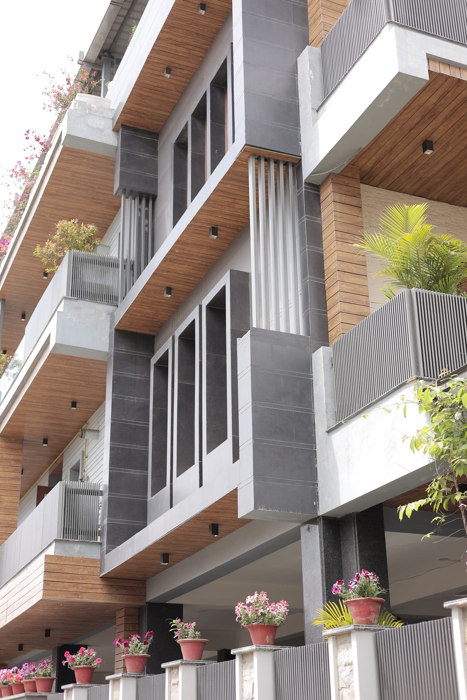 Elevated view of the terraces showing grey stone parapets, timber-clad walls, planter boxes and rows of potted flowers in daylight.